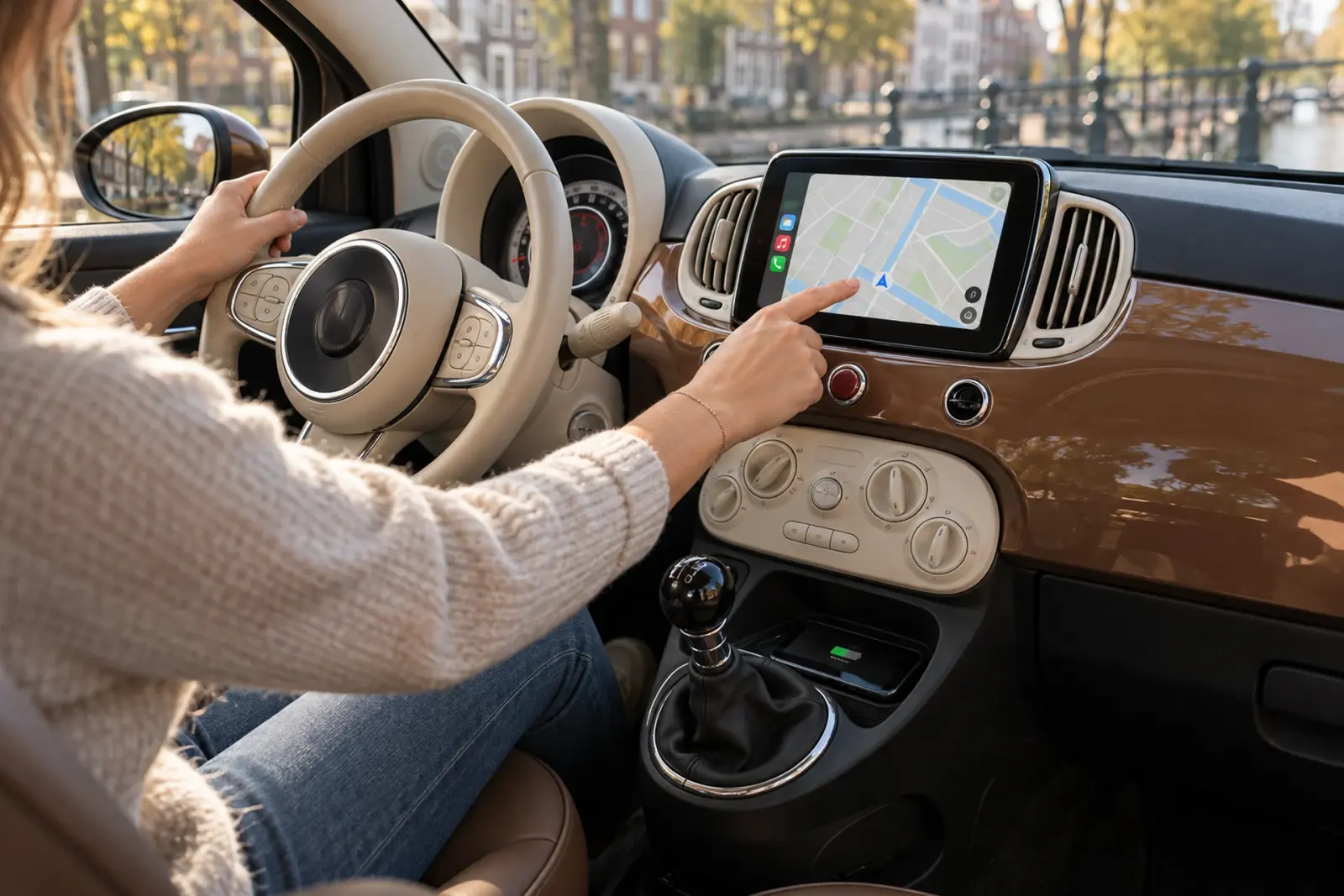 Bestuurder bedient de navigatie op een ingebouwd CarPlay-scherm in een Fiat 500 langs een gracht in Haarlem